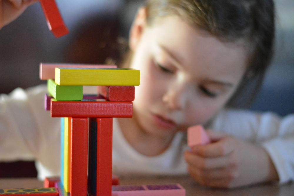 Tyttö rakentaa värillisistä puupalikoista tornia pöydän ääressä