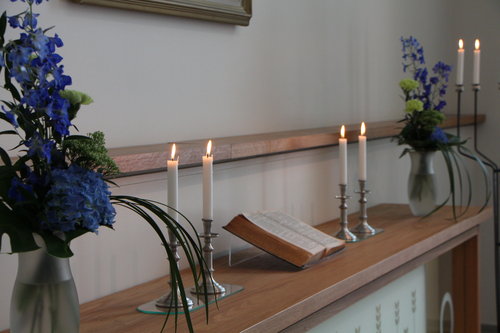 Huutijärven kappelin puisella alttarilla raamattu, valkoiset kynttilät ja siniset kukat.