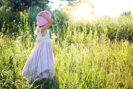 Lapsi seisoo kesämekossa ja kesähattu päässä heinäpellolla auringon paisteessa.