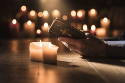 Henkilö lukee Raamattua kynttilöiden valossa