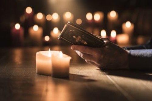 Kynttilöitä ja raamattua lukevan henkilön kädet ja raamattu.