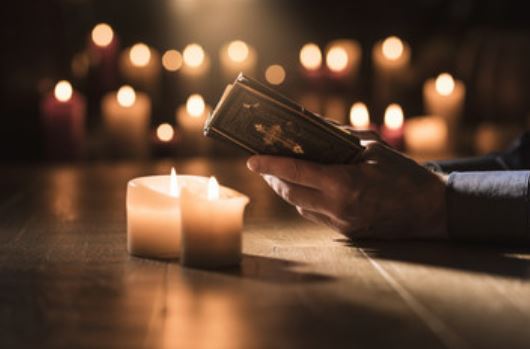 kynttilöitä, raamattu ja kädet, jotka pitelevät raamattua.