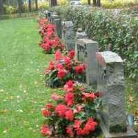 Seurakunnan hoidossa olevia hautoja. Punaisia kukkia hautakivien edessä.