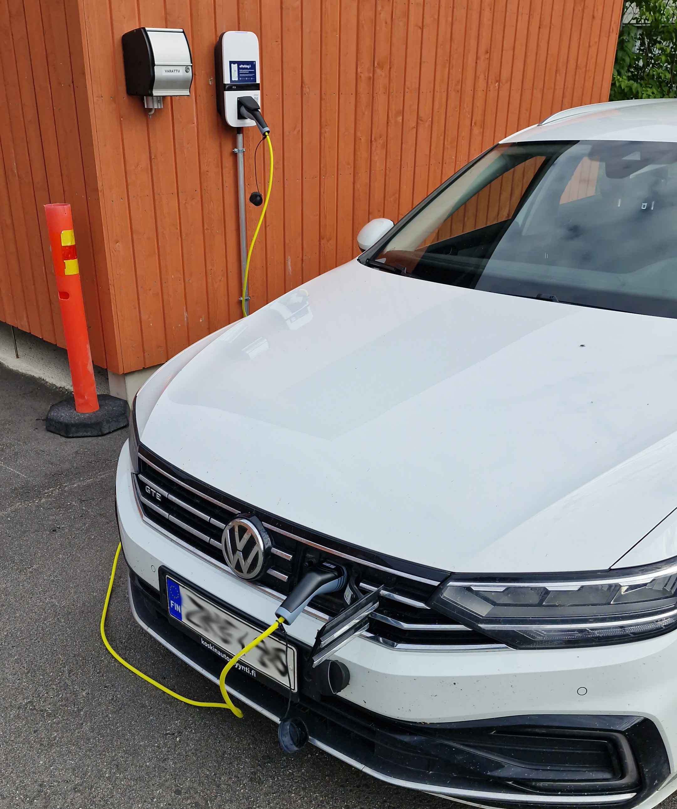 Lähikuva latauspisteeseen kytketyn valkoisen auton keulasta.